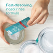 Load image into Gallery viewer, Contents of the nasal rinse sachet being poured into a clear container with other containers beside it showing the before and after picture of the contents being dissolved