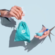 Load image into Gallery viewer, Hand holding a drawstring storage bag and the other hand holding microwavable cup and metal applicator