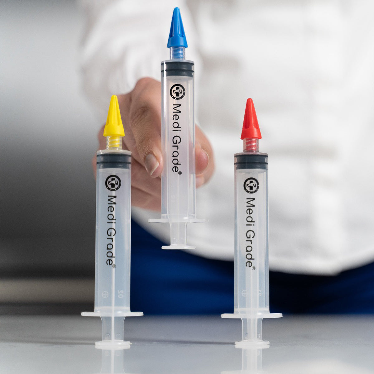 3 Medi Grade Earwax Removal Syringes on a table while the middle ear syringe is being picked up by a person