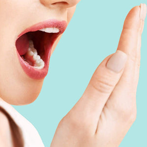 A woman is holding her mouth open and smelling her breath